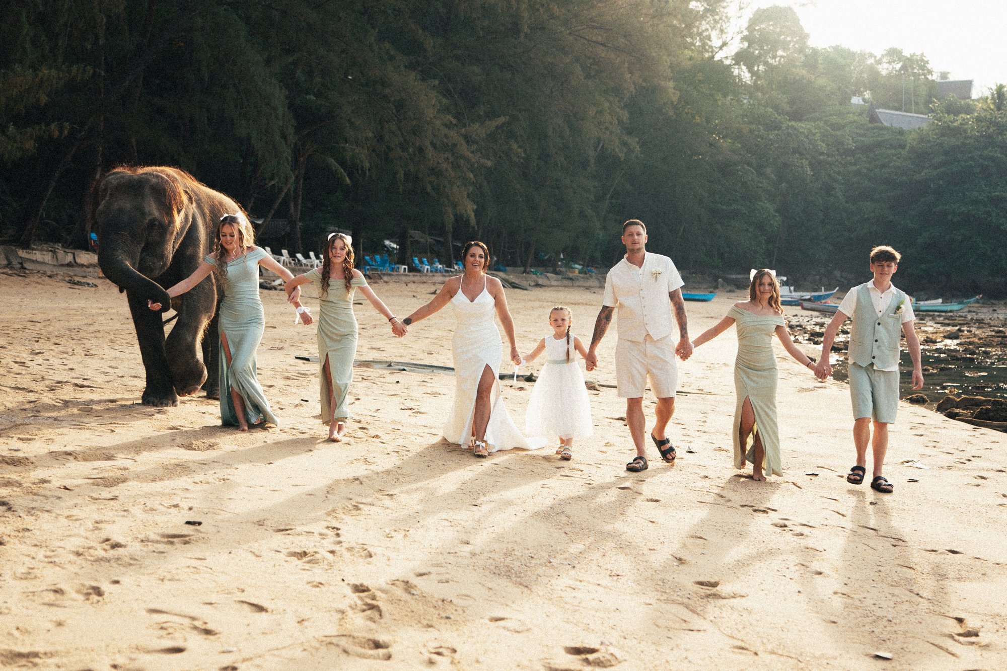 Jade and Nicky walking hand-in-hand down Hua Beach with their small wedding party after the ceremony, sunlight low across the sand