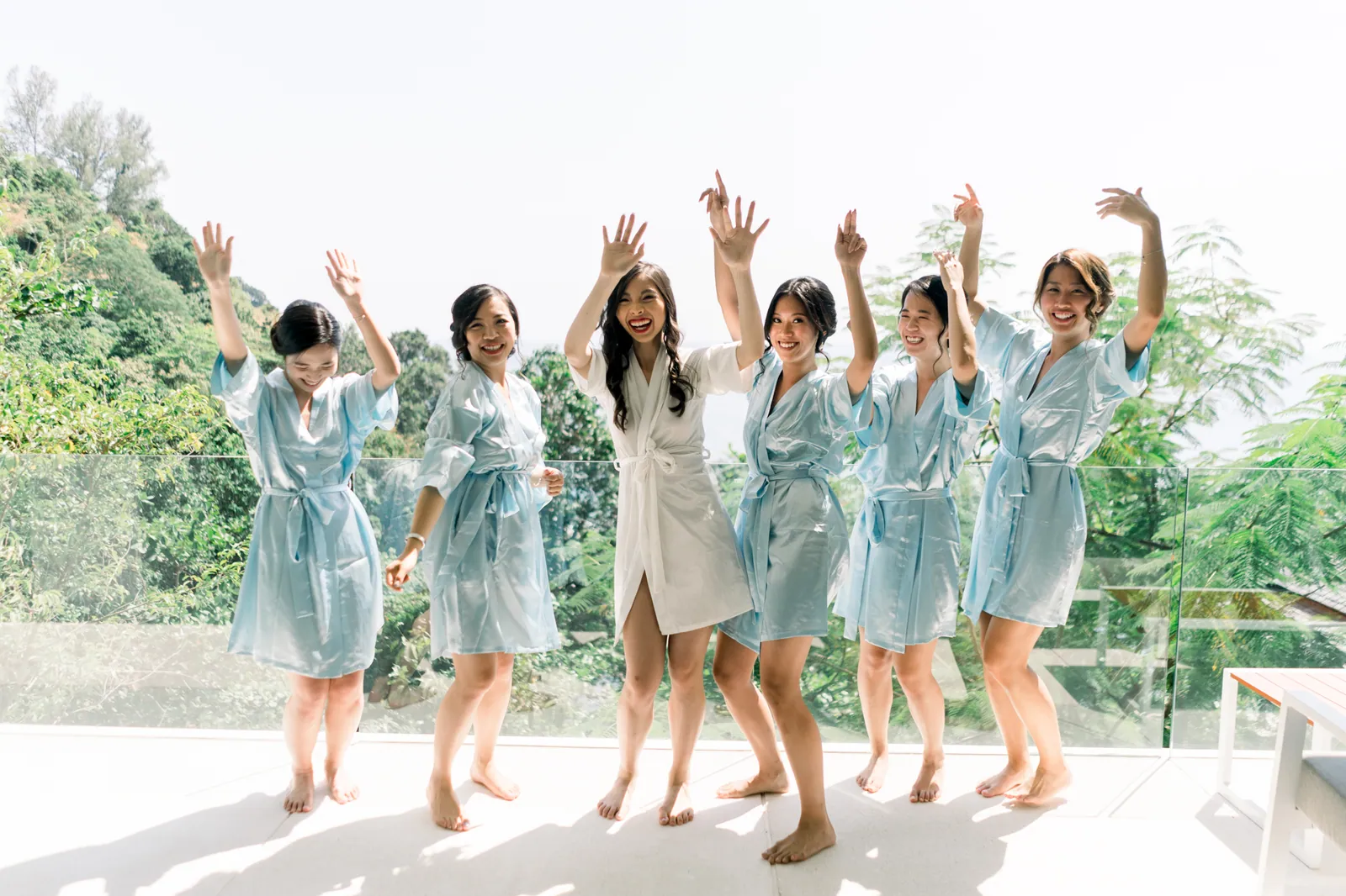 Eunice and her bridesmaids in matching dusty blue robes on the villa terrace, hands raised