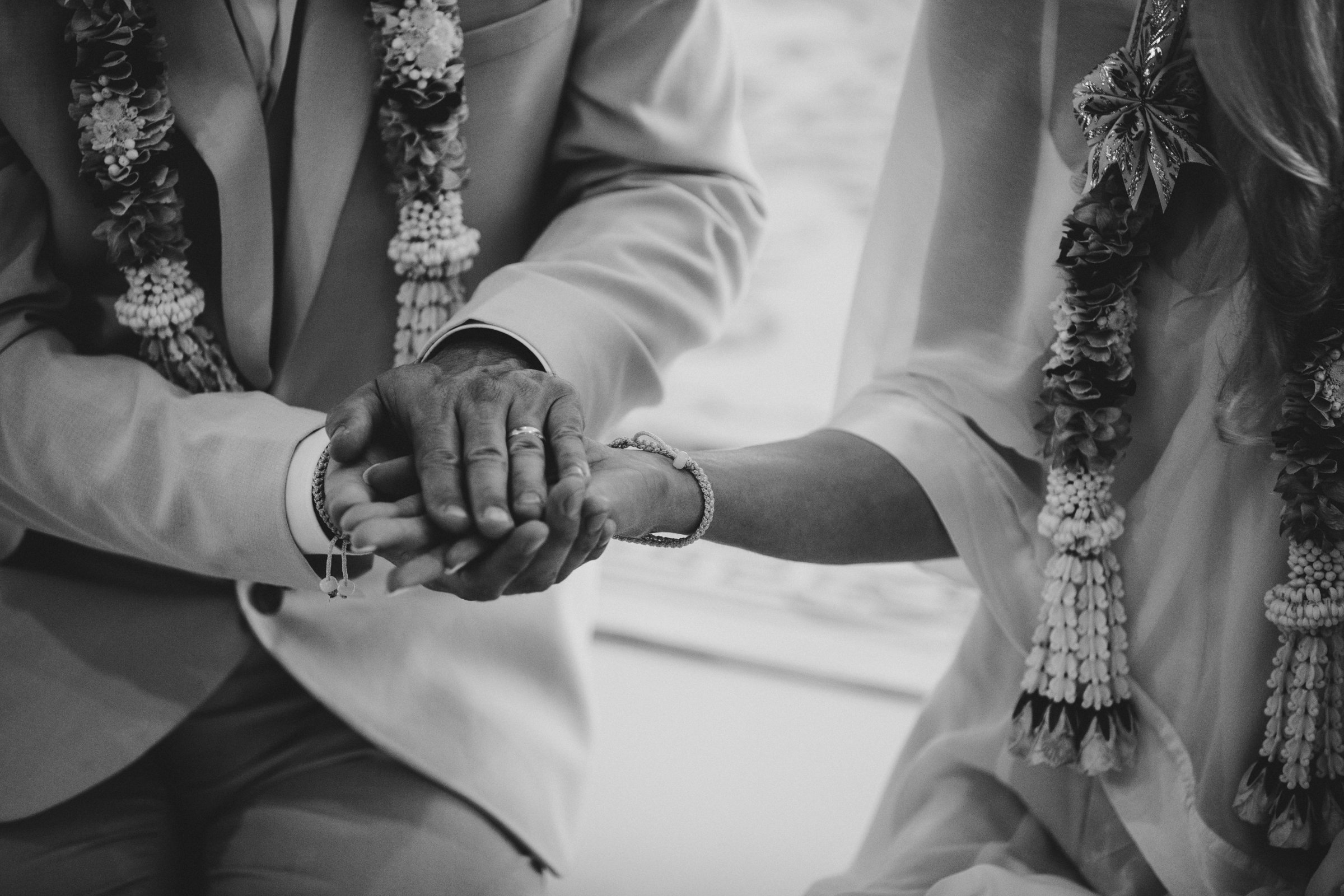 Anne and Jeremy holding hands after the tying of the sai sin thread, in black and white