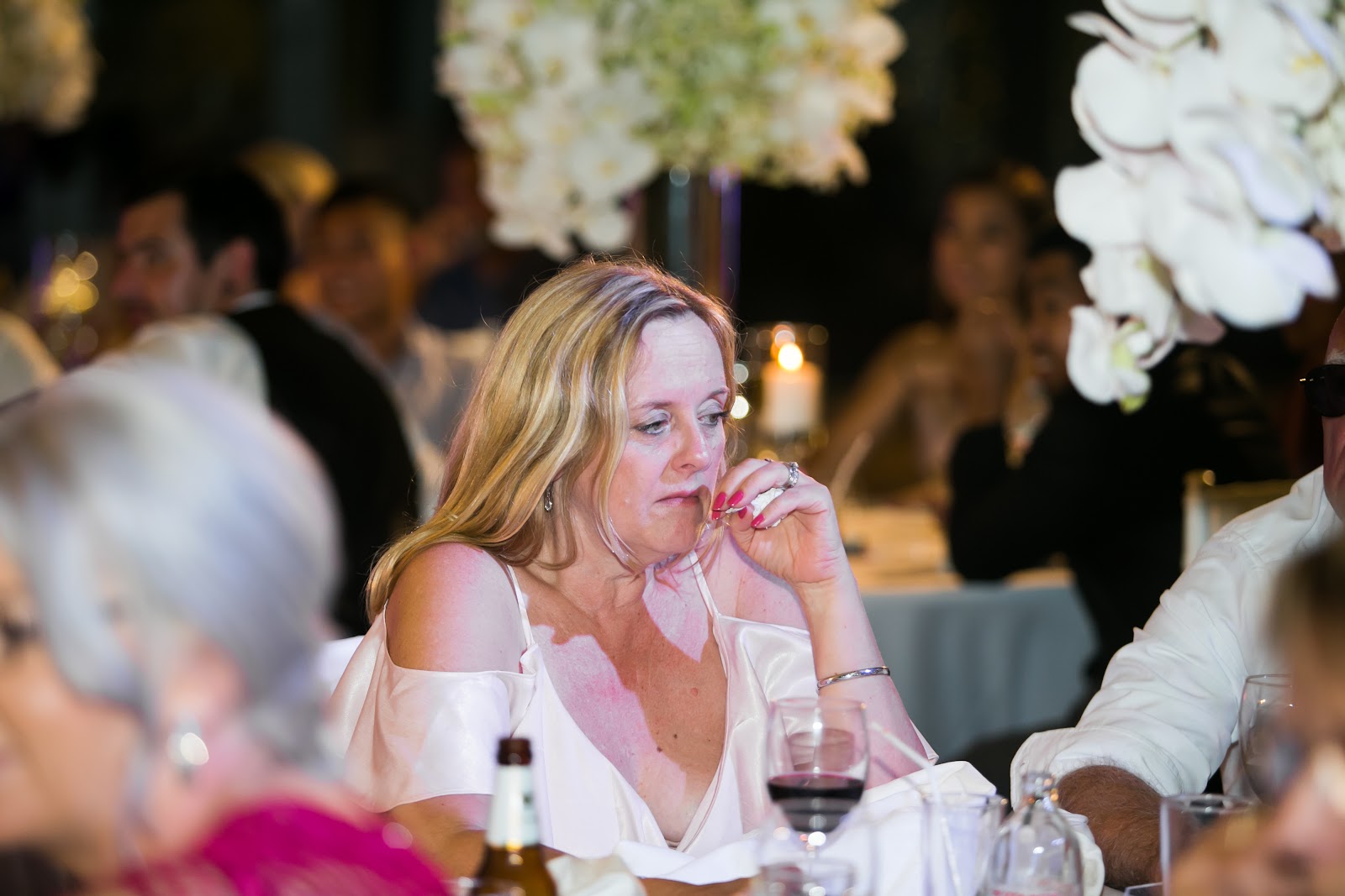 A guest listens through a speech at the candlelit reception, white orchid centrepieces framing the moment