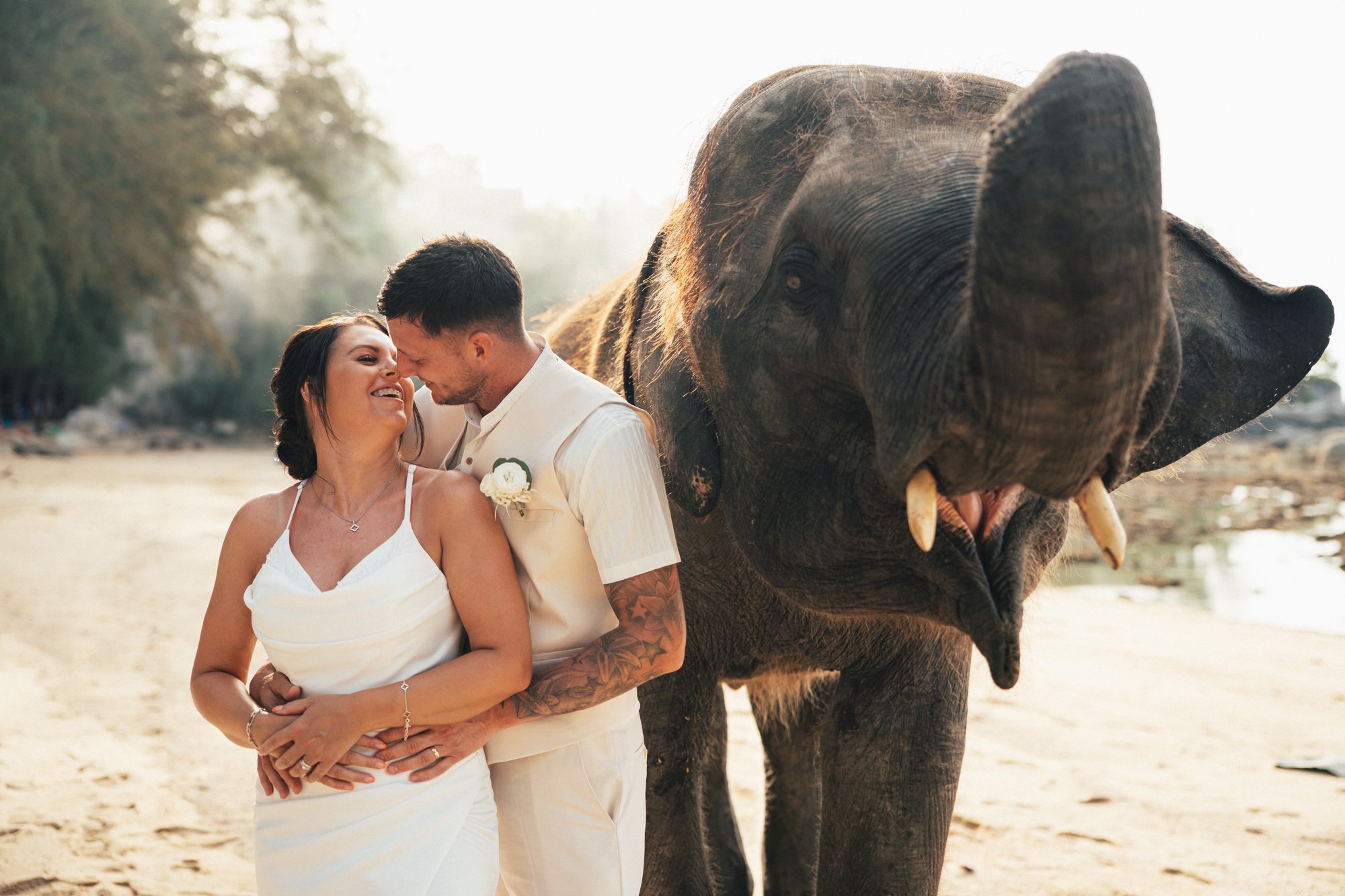 Jade and Nicky embracing on Hua Beach with the young elephant close beside them