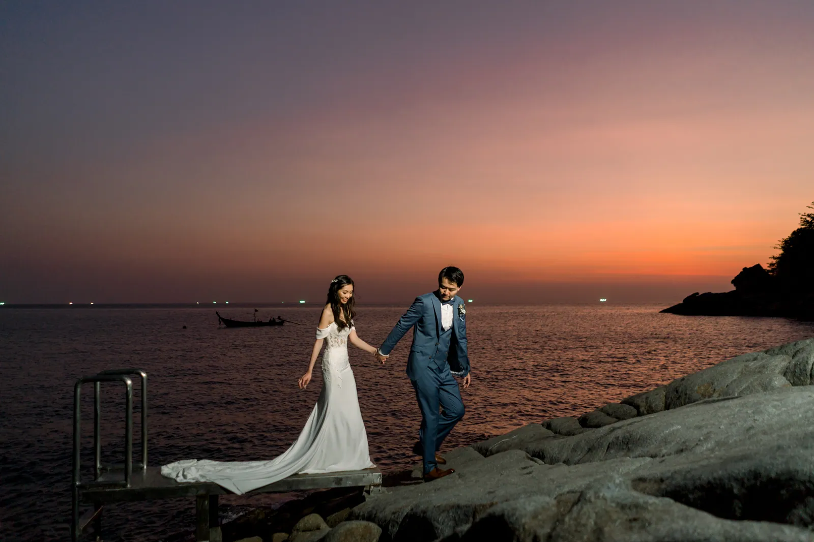 Eunice and Ryan on the rocks below Villa Aquila as the sky turns orange and violet at sunset