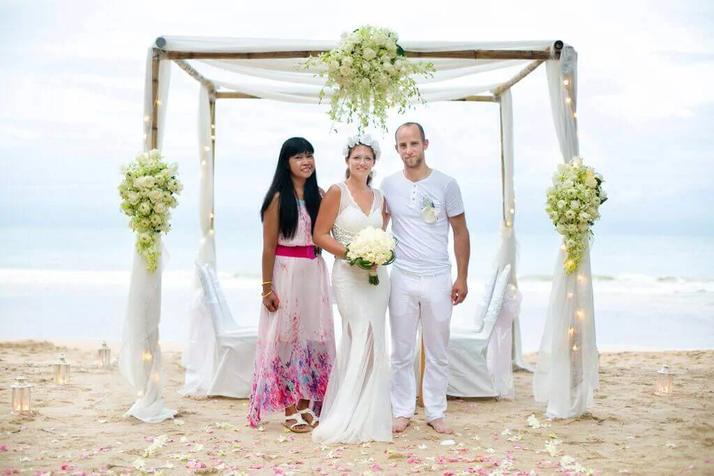 A beach wedding ceremony on Phuket with a floral arch and seated guests at the shoreline.