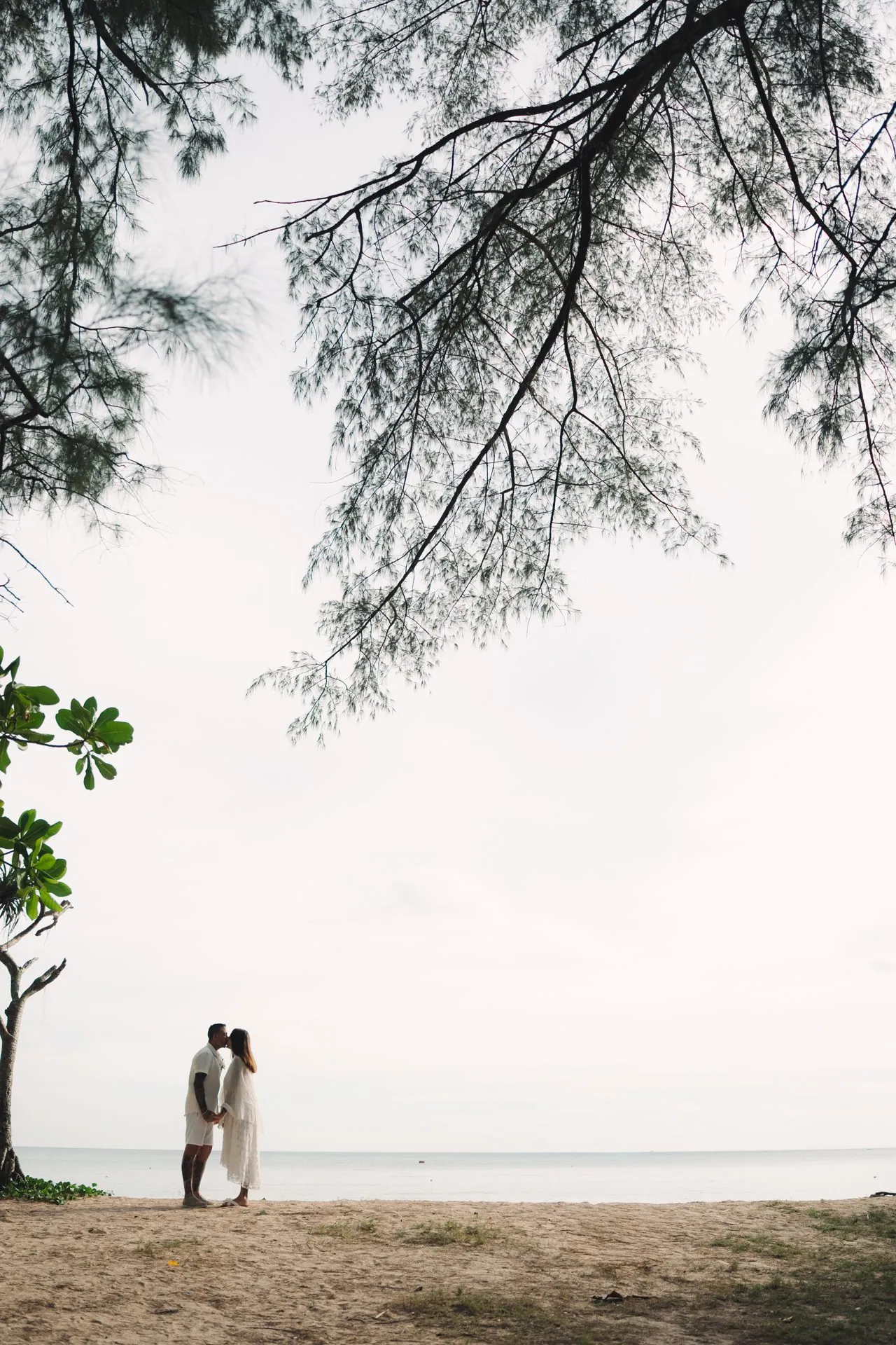 Distant silhouette of Joanne and Richard on the empty sand at Layan Beach, framed by overhanging trees