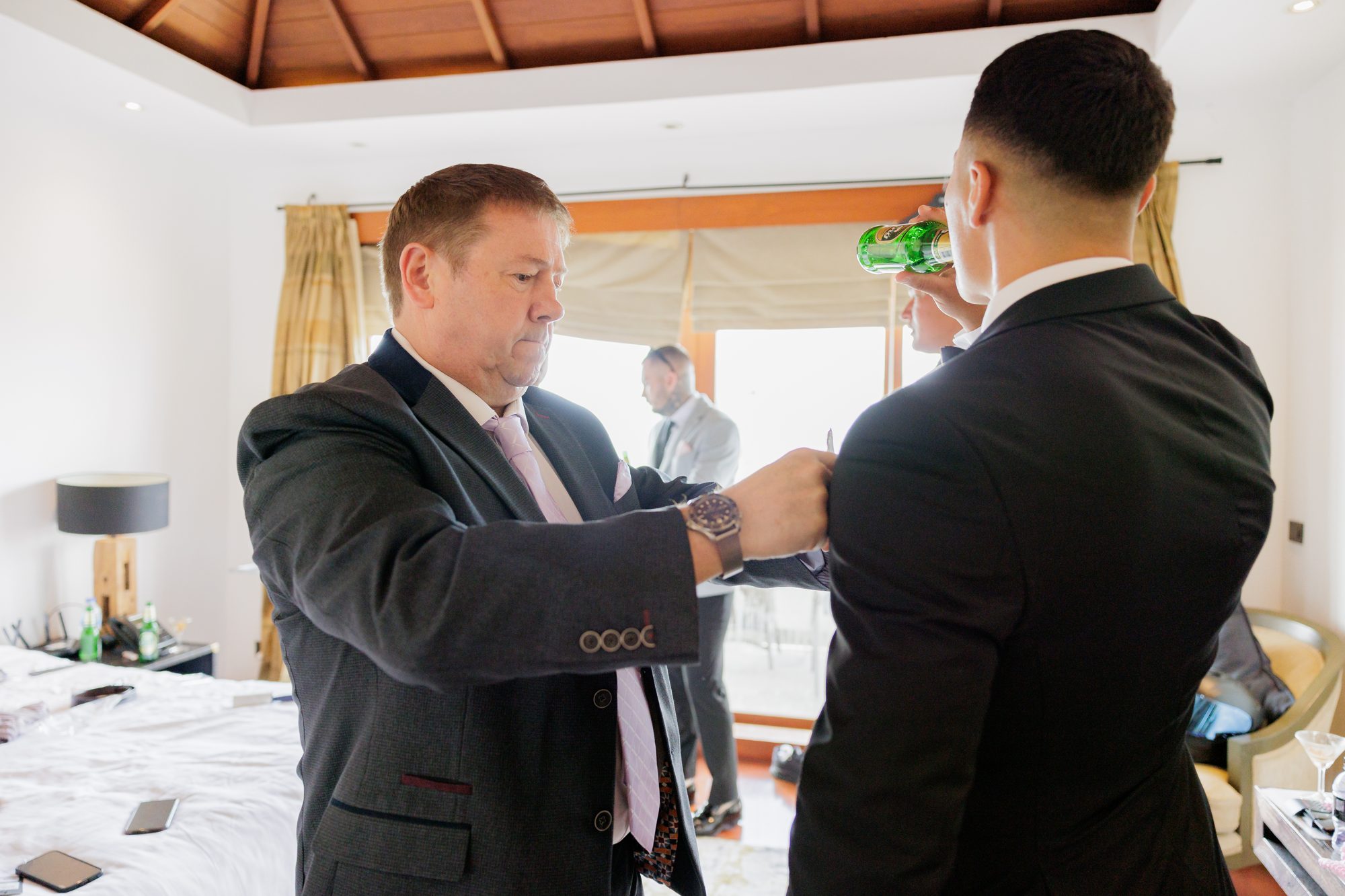 James having his tie adjusted by a groomsman in the villa suite before the ceremony