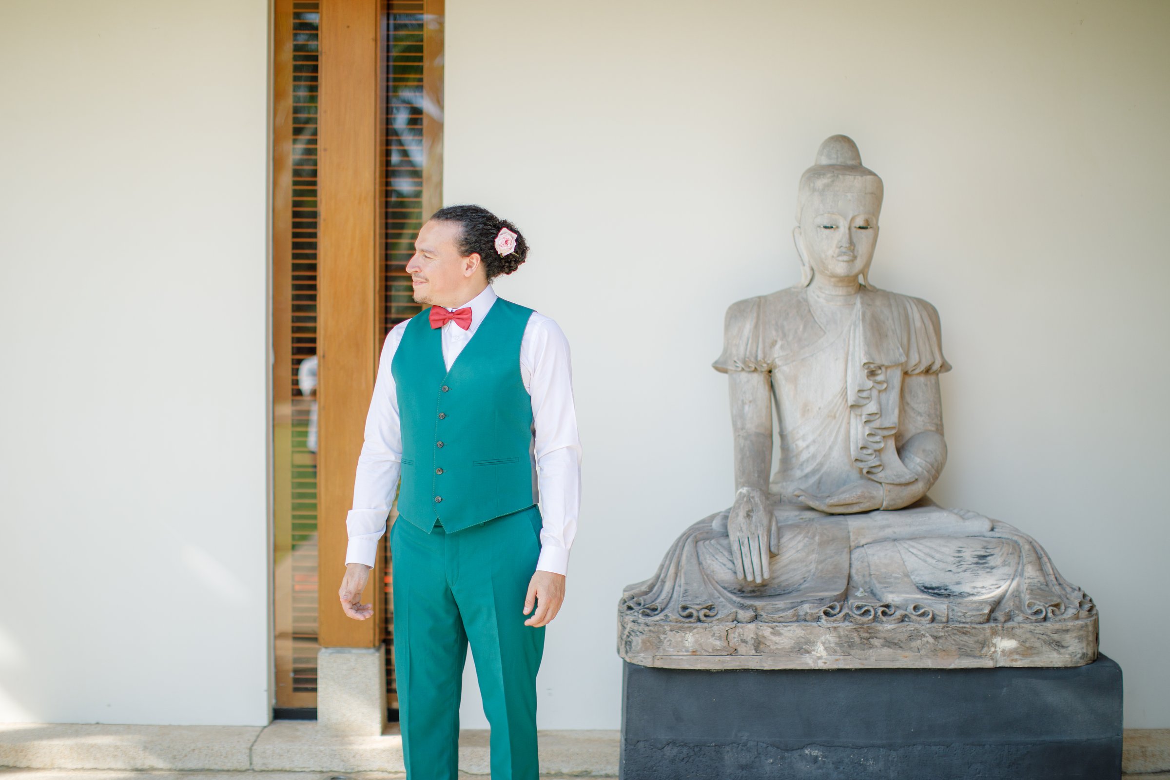 Victor in an emerald-green suit and coral bow tie beside a stone Buddha at Villa Shanti