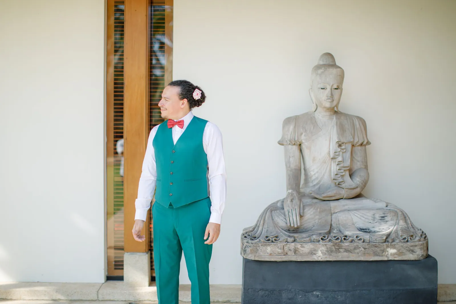 Victor in an emerald-green suit and coral bow tie beside a stone Buddha at Villa Shanti