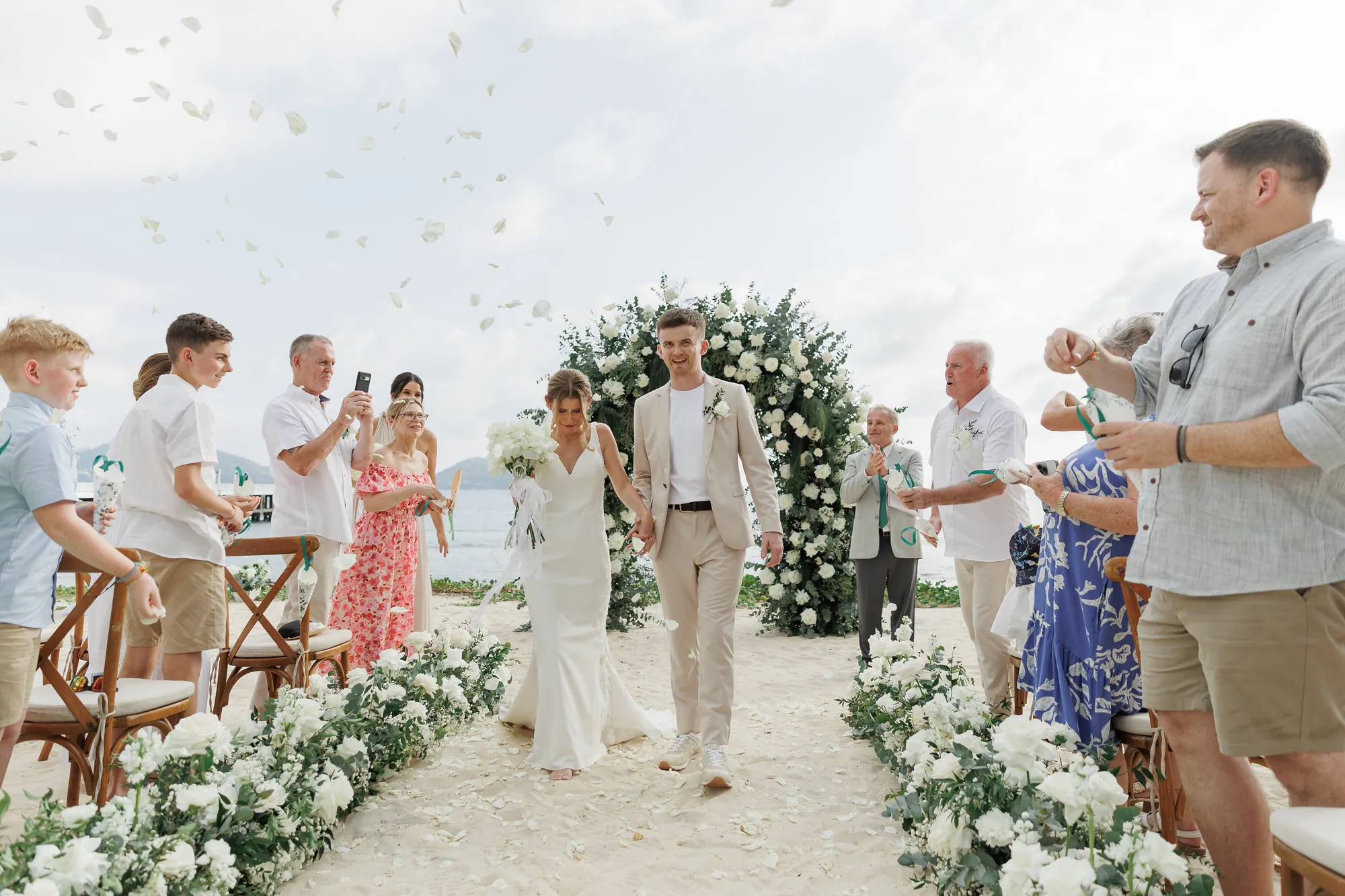 A beach wedding ceremony on Phuket with a floral arch and seated guests at the shoreline.