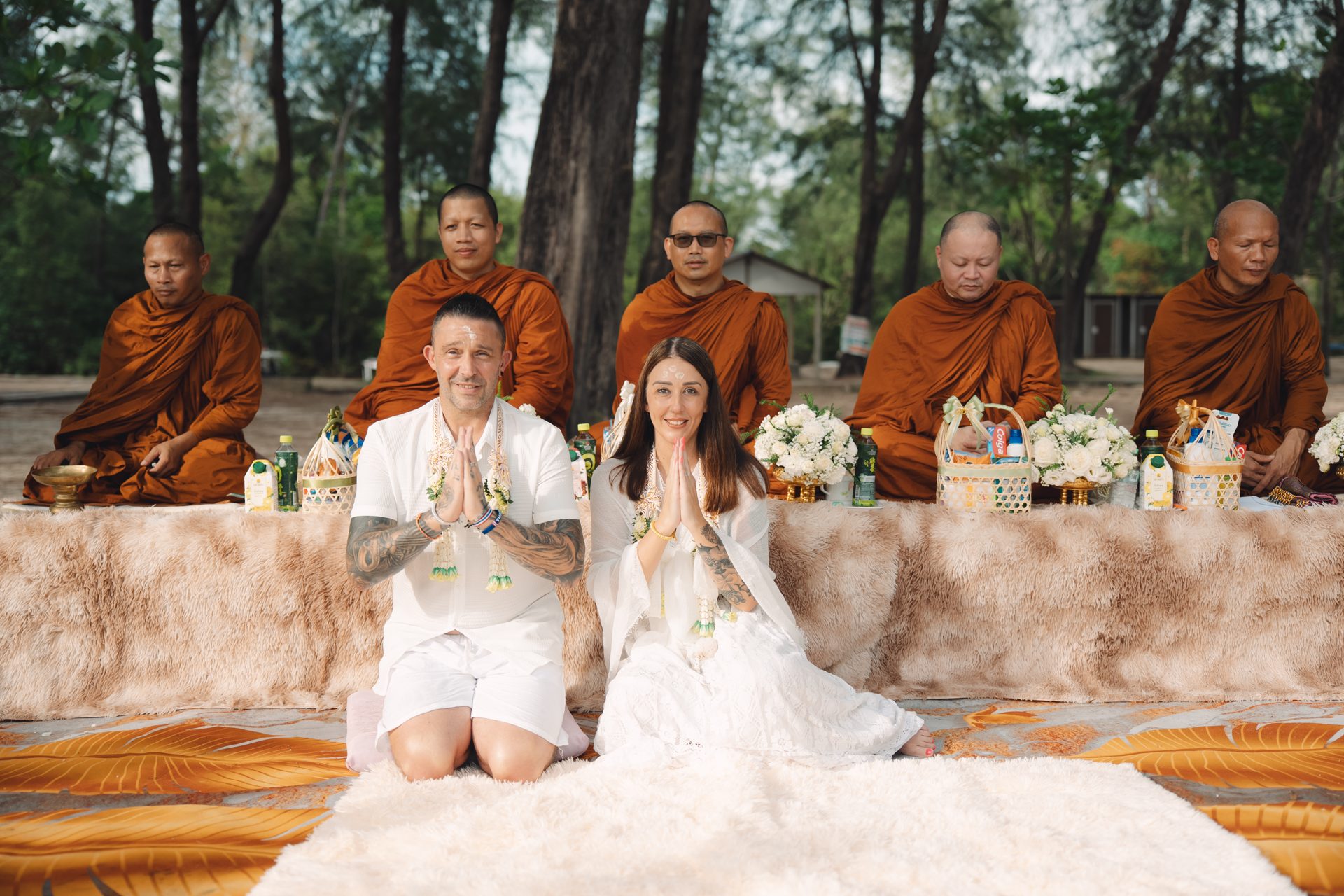 Joanne and Richard in white with hands together in wai, receiving the blessing from the five monks on Layan Beach
