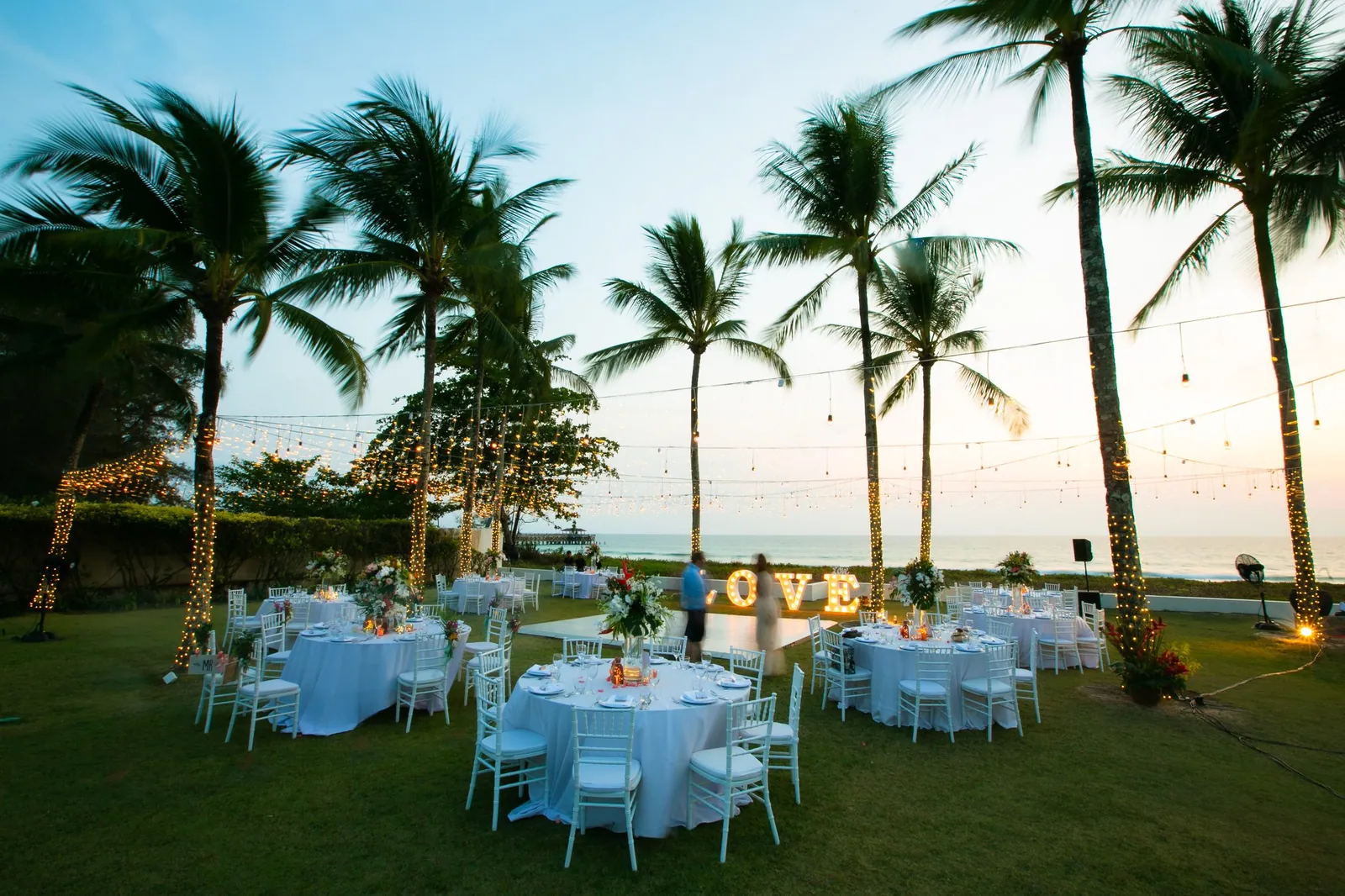 Dinner tables set on the lawn at Villa Jia at dusk with a lit LOVE sign for Bekki and Glen's reception