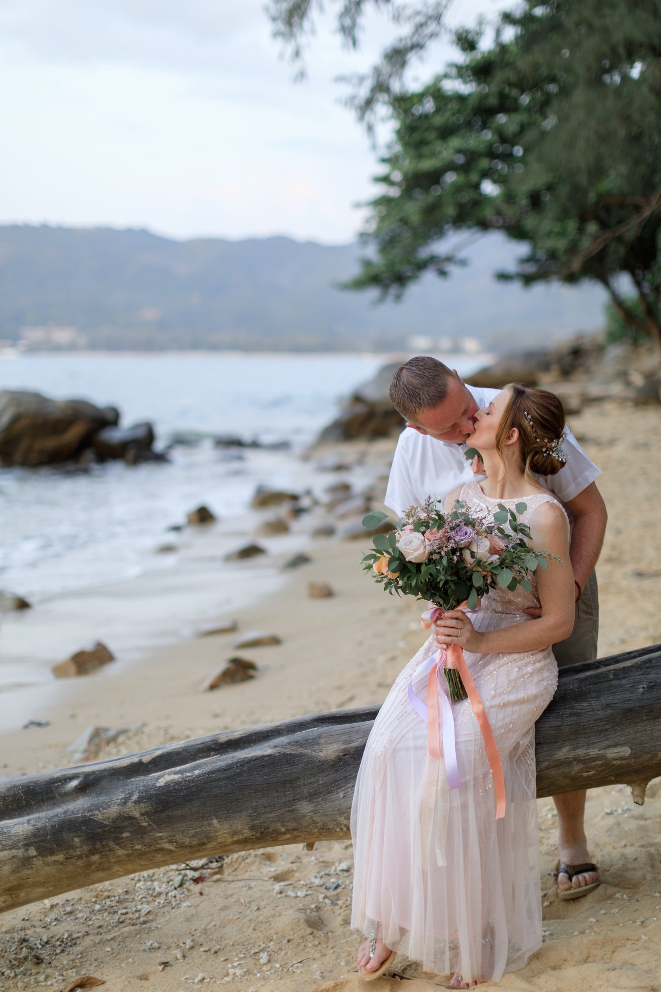 Amanda and John in a quiet portrait embrace on the rocks at Hua Beach after their ceremony