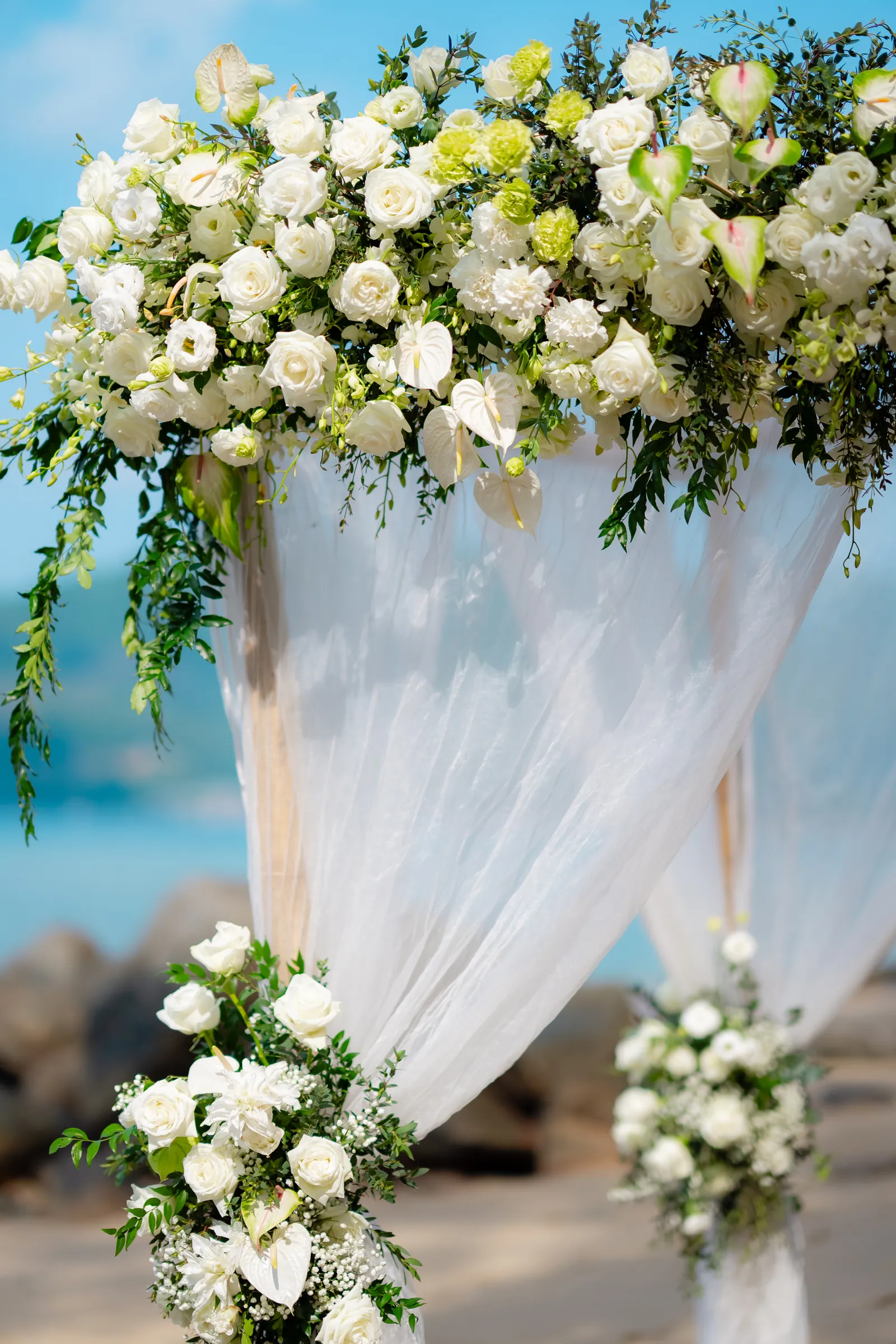 The finished bamboo flower archway on Hua Beach, draped in soft white fabric with clusters of white roses, calla lilies and green foliage on either post