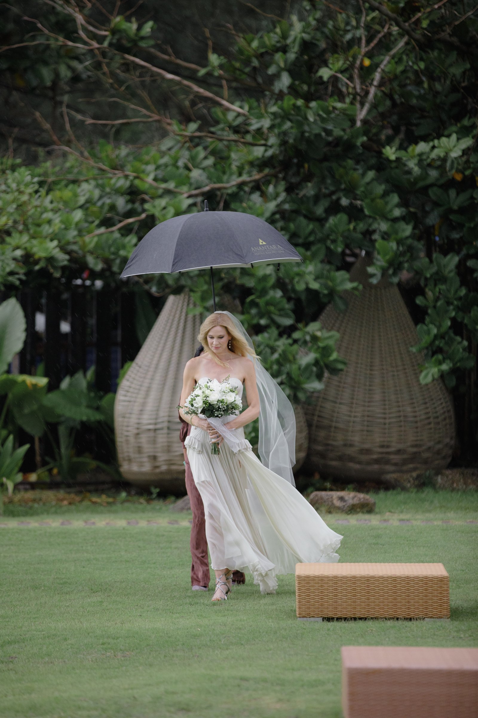 Anne walking through the gardens at Anantara Mai Khao towards the beach with a white umbrella