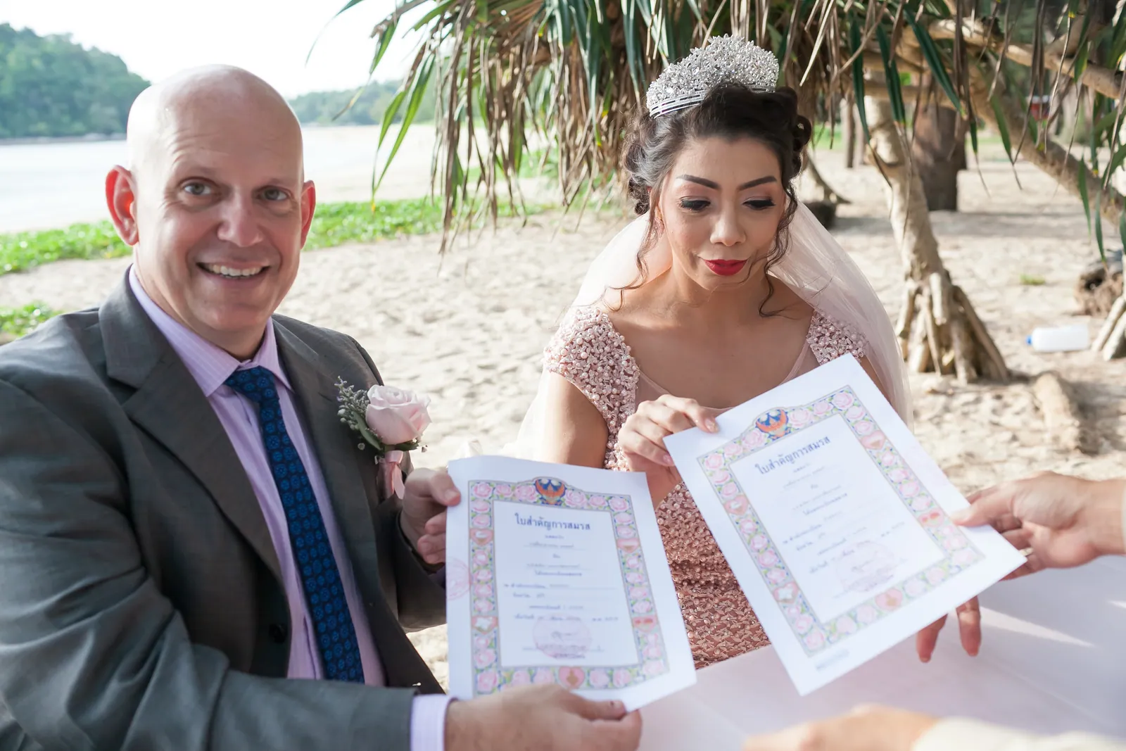 Doug and Parisa holding their Thai marriage certificates (ใบสำคัญการสมรส) on Layan Beach after the legal signing