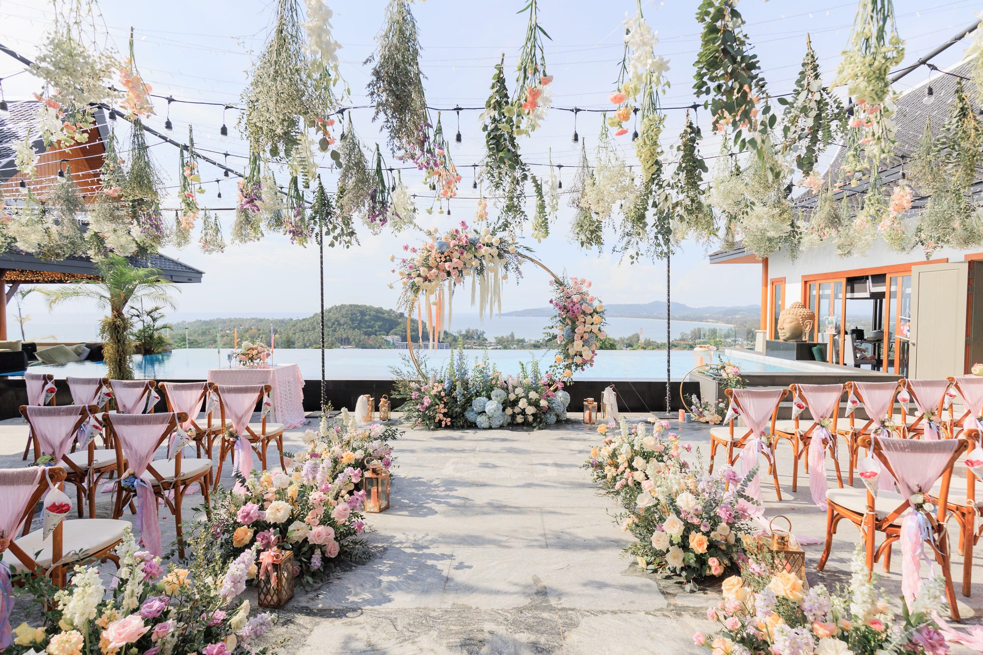 The ceremony aisle at Villa Baan Phu Prana on the morning of Ashleigh and James's wedding, with pastel florals and hanging installations framing the sea beyond
