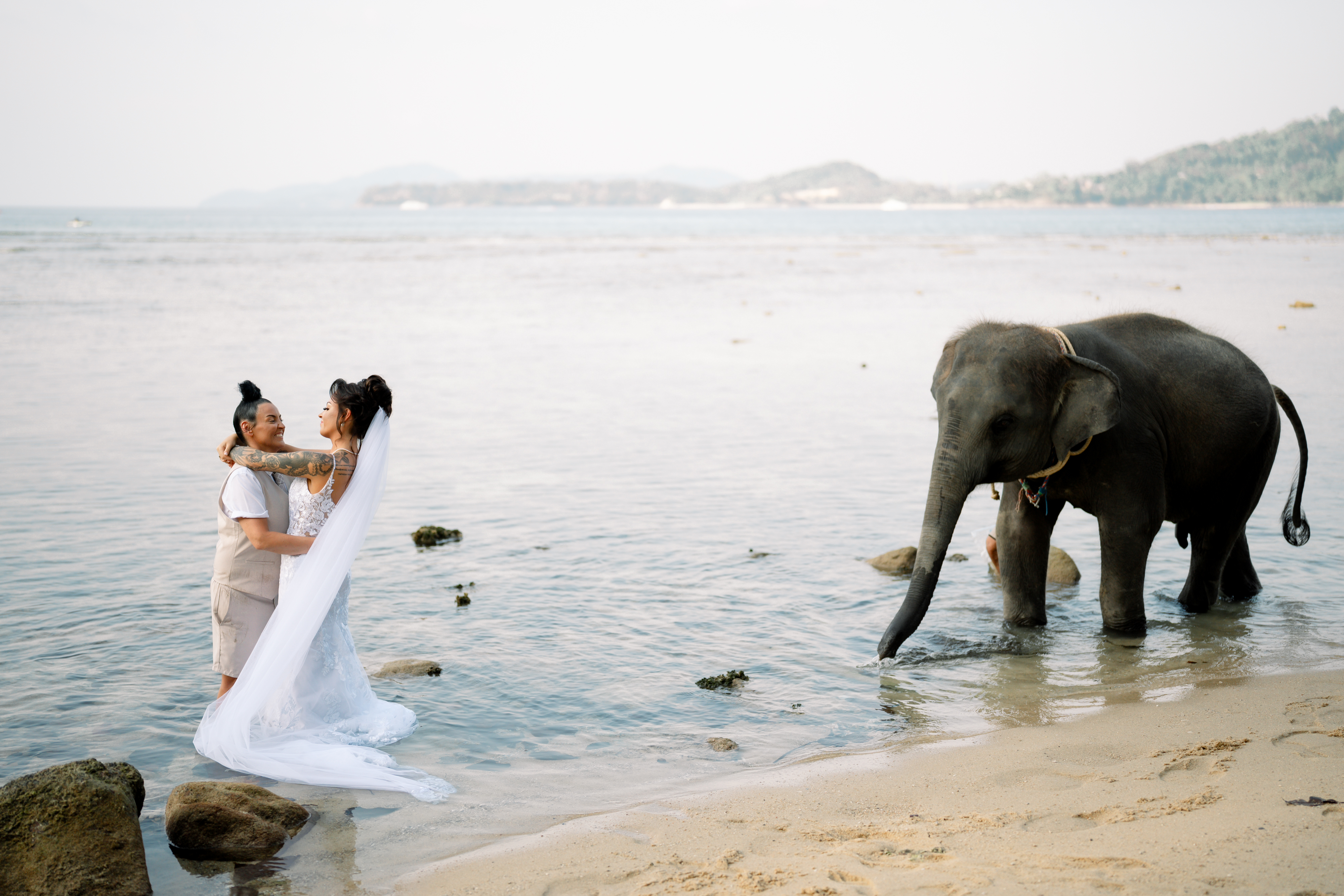 Gemma and Rebecca standing in the shallows on Hua Beach beside the baby elephant walking out into the water beside them