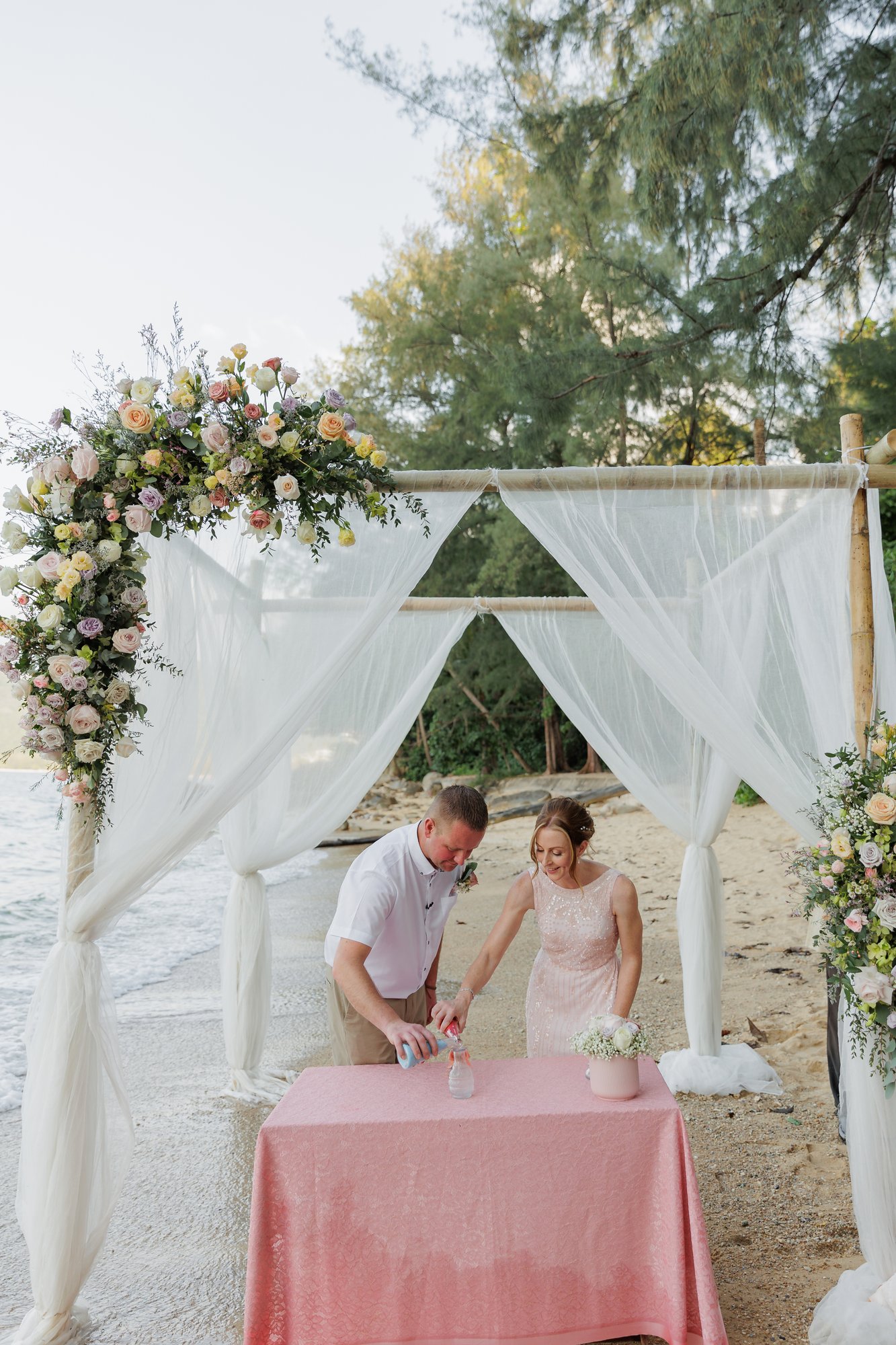 Amanda and John pouring red and blue sand together during the unity sand ritual at their Hua Beach wedding ceremony