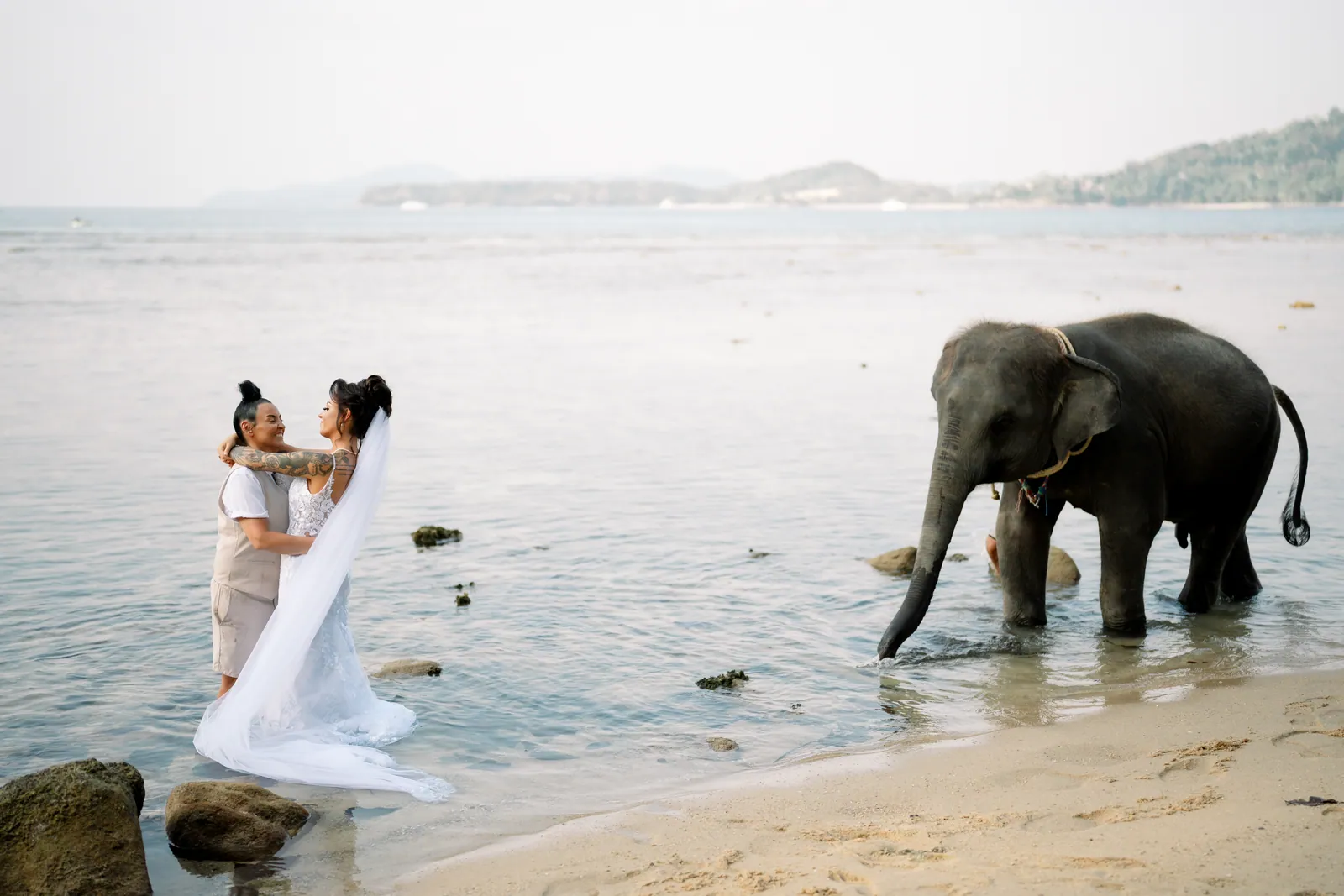 Gemma and Rebecca standing in the shallows on Hua Beach beside the baby elephant walking out into the water beside them