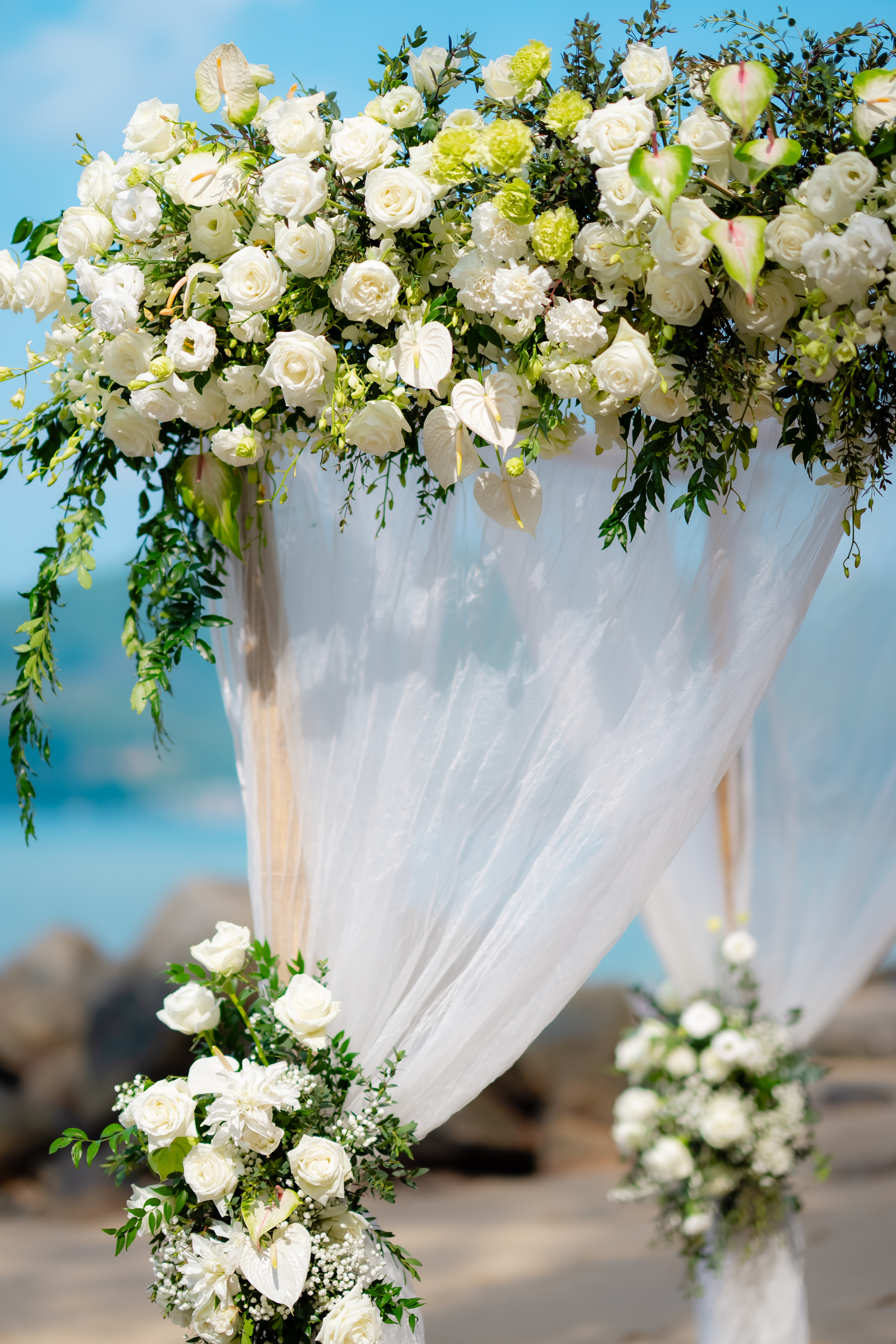 The finished bamboo flower archway on Hua Beach, draped in soft white fabric with clusters of white roses, calla lilies and green foliage on either post