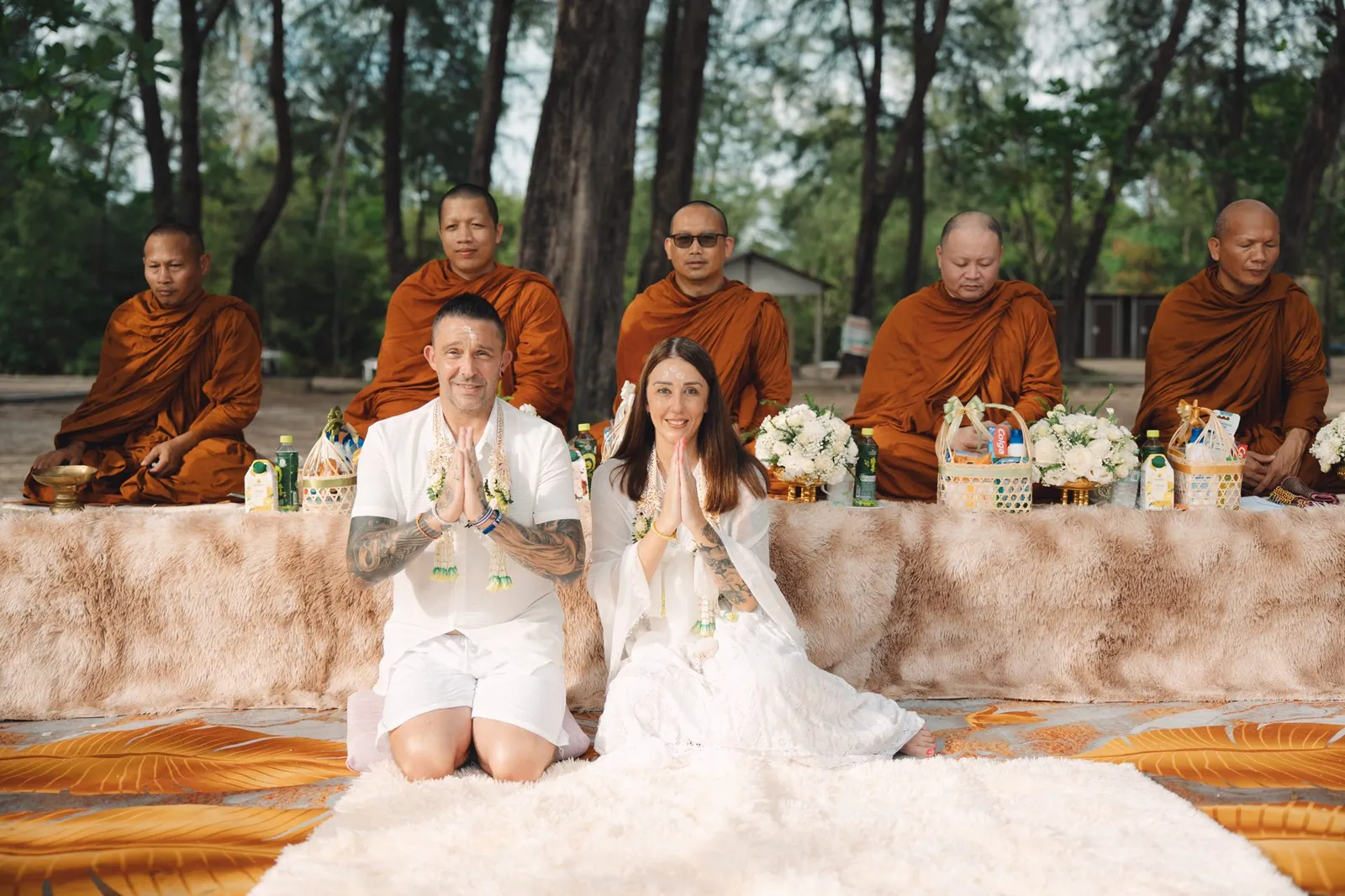 Joanne and Richard in white with hands together in wai, receiving the blessing from the five monks on Layan Beach