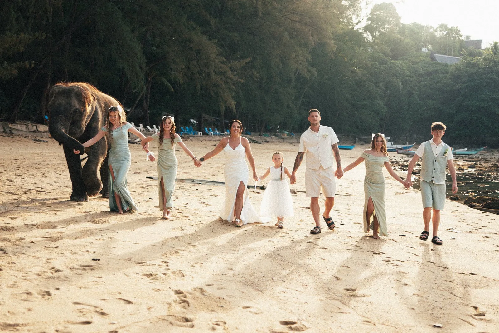 Jade and Nicky walking hand-in-hand down Hua Beach with their small wedding party after the ceremony, sunlight low across the sand