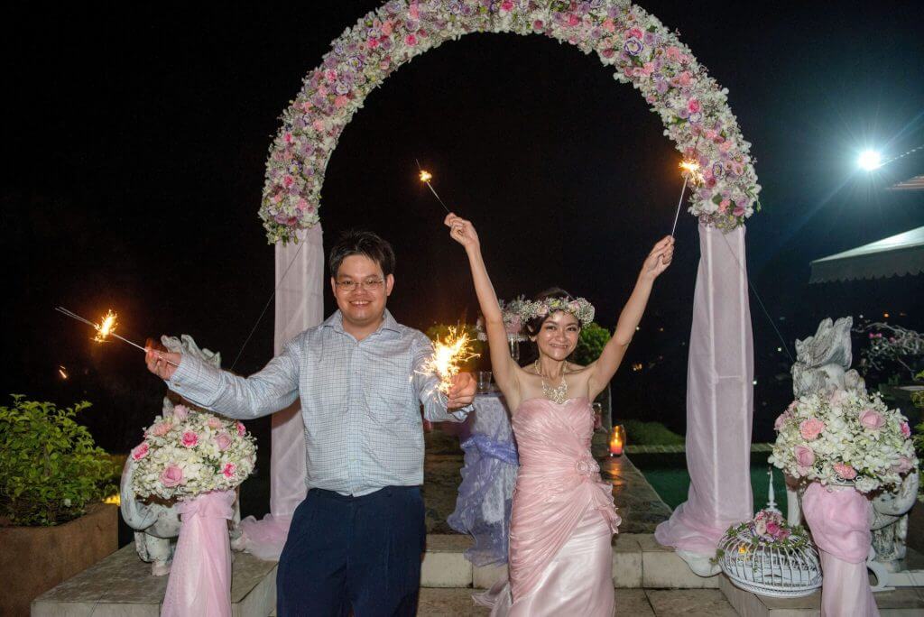 George and Gan Wan Wei celebrating with sparklers in front of the wedding arch at night