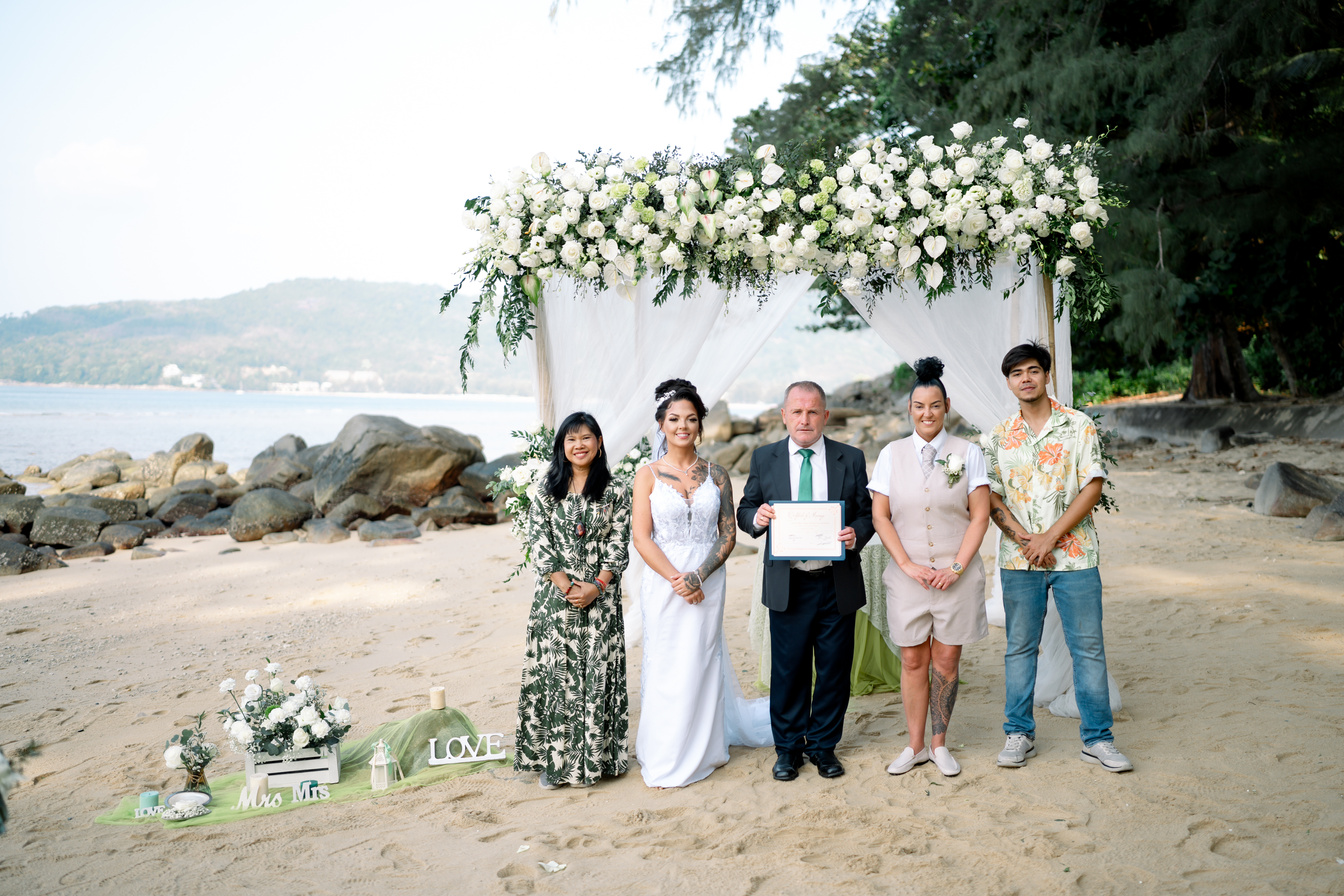 Gemma and Rebecca beneath the arch with their celebrant and the two Thai witnesses required for the ceremony, holding the signed marriage document up together