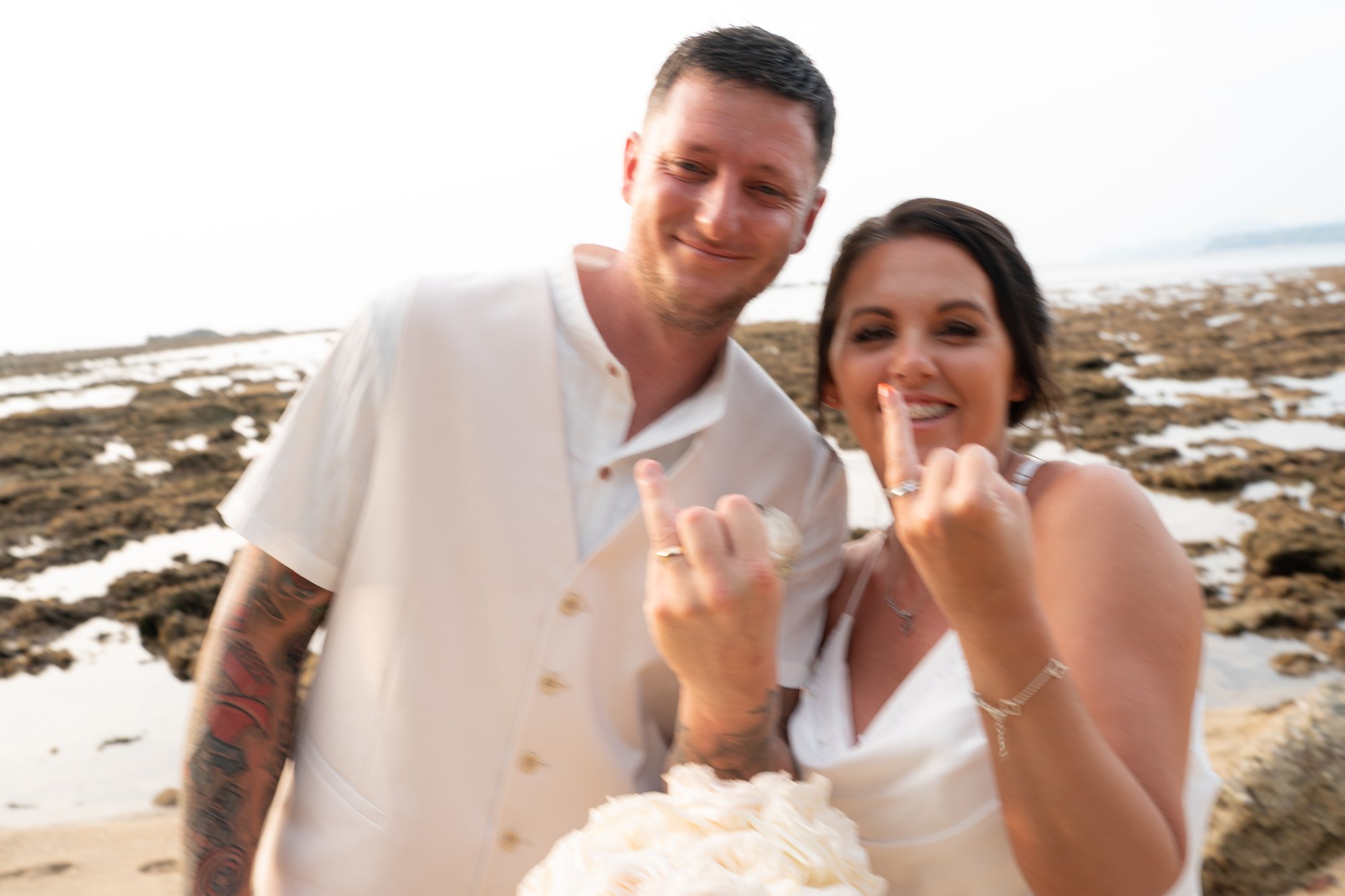 Jade and Nicky in close portrait on the beach, showing off her wedding ring and both smiling