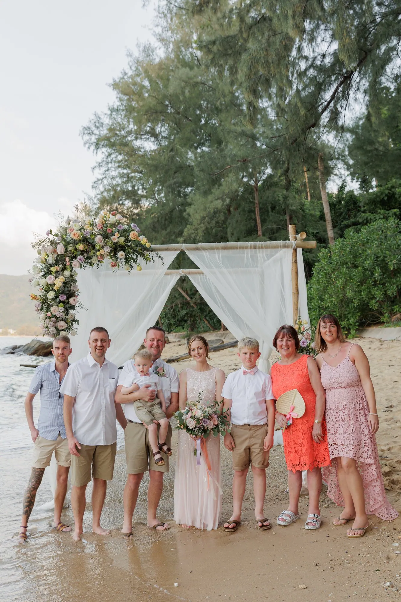 Amanda and John with their family and friends gathered under the ceremony arch at Hua Beach for a group portrait