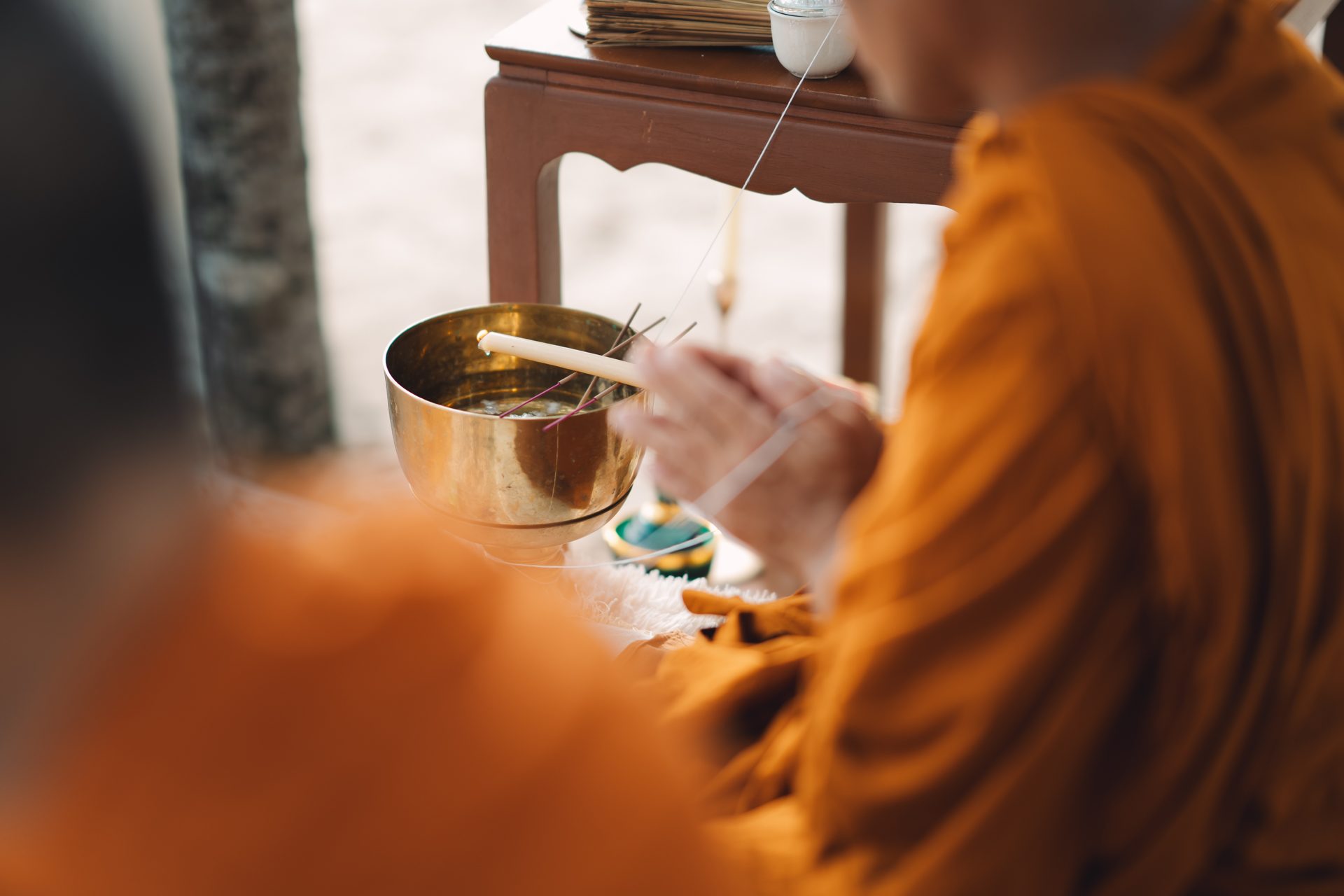 A monk in saffron robes holding a small brass singing bowl during Joanne and Richard's Layan Beach blessing
