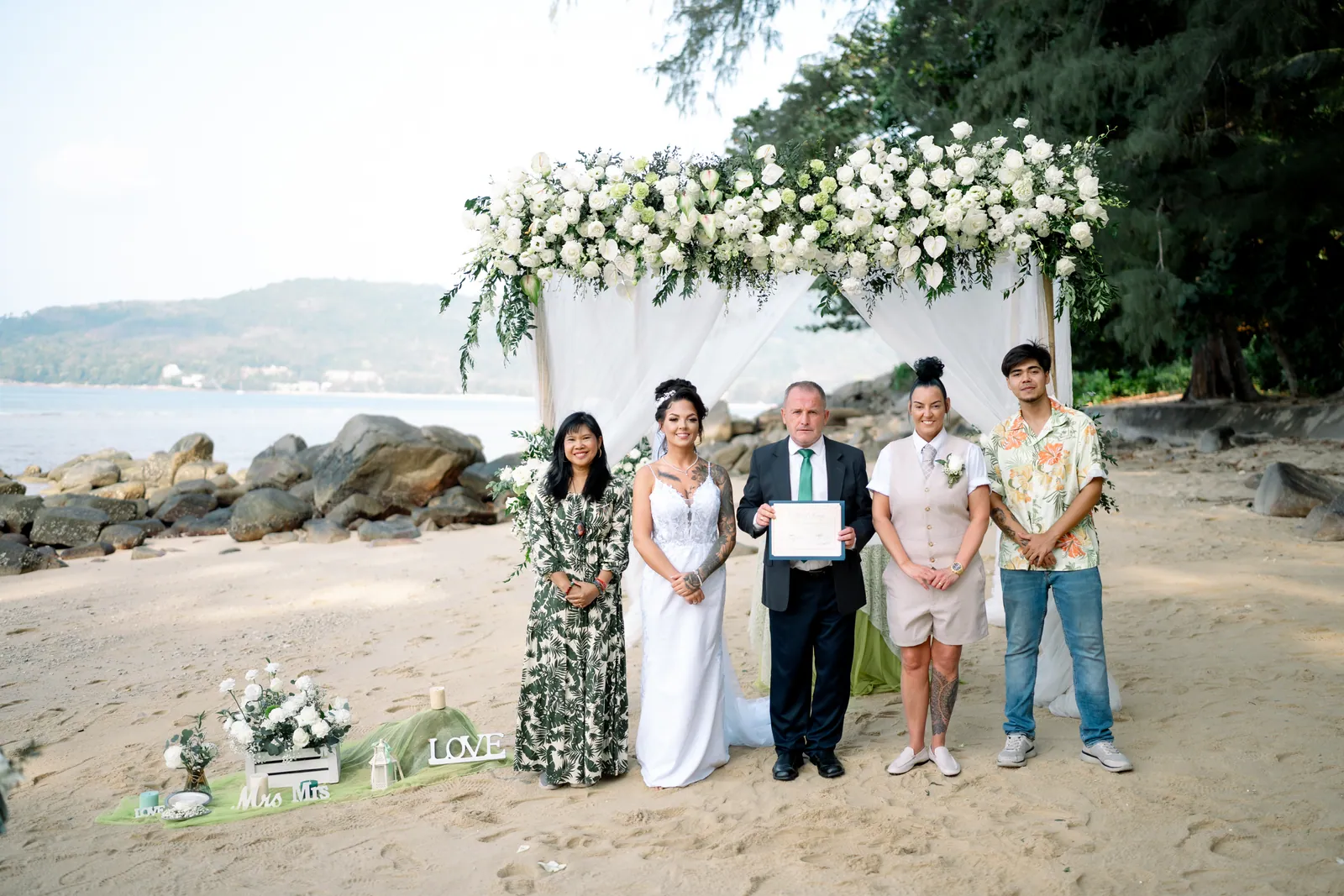 Gemma and Rebecca beneath the arch with their celebrant and the two Thai witnesses required for the ceremony, holding the signed marriage document up together