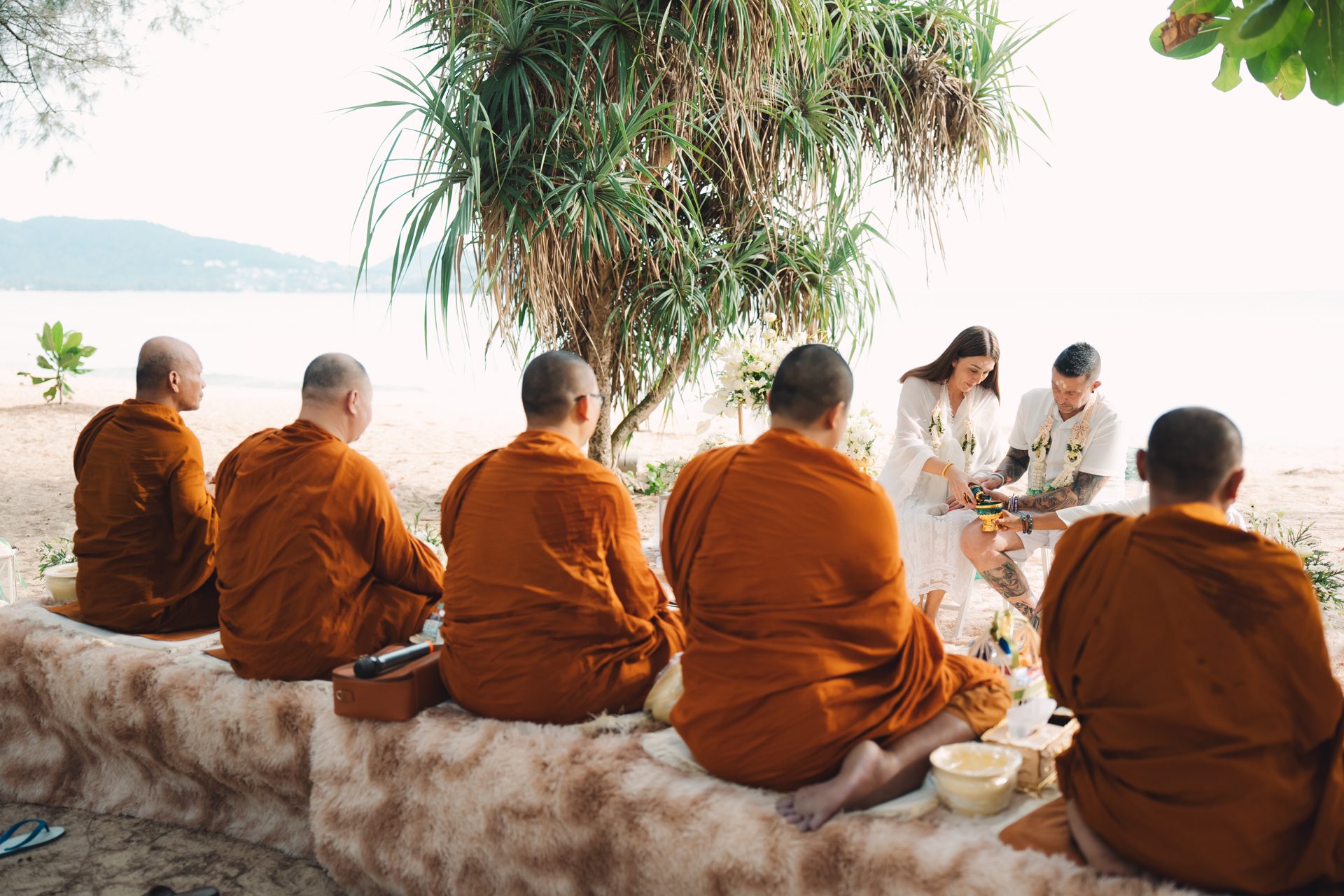 Joanne and Richard seated on the sand at Layan Beach in front of the five Buddhist monks during the blessing