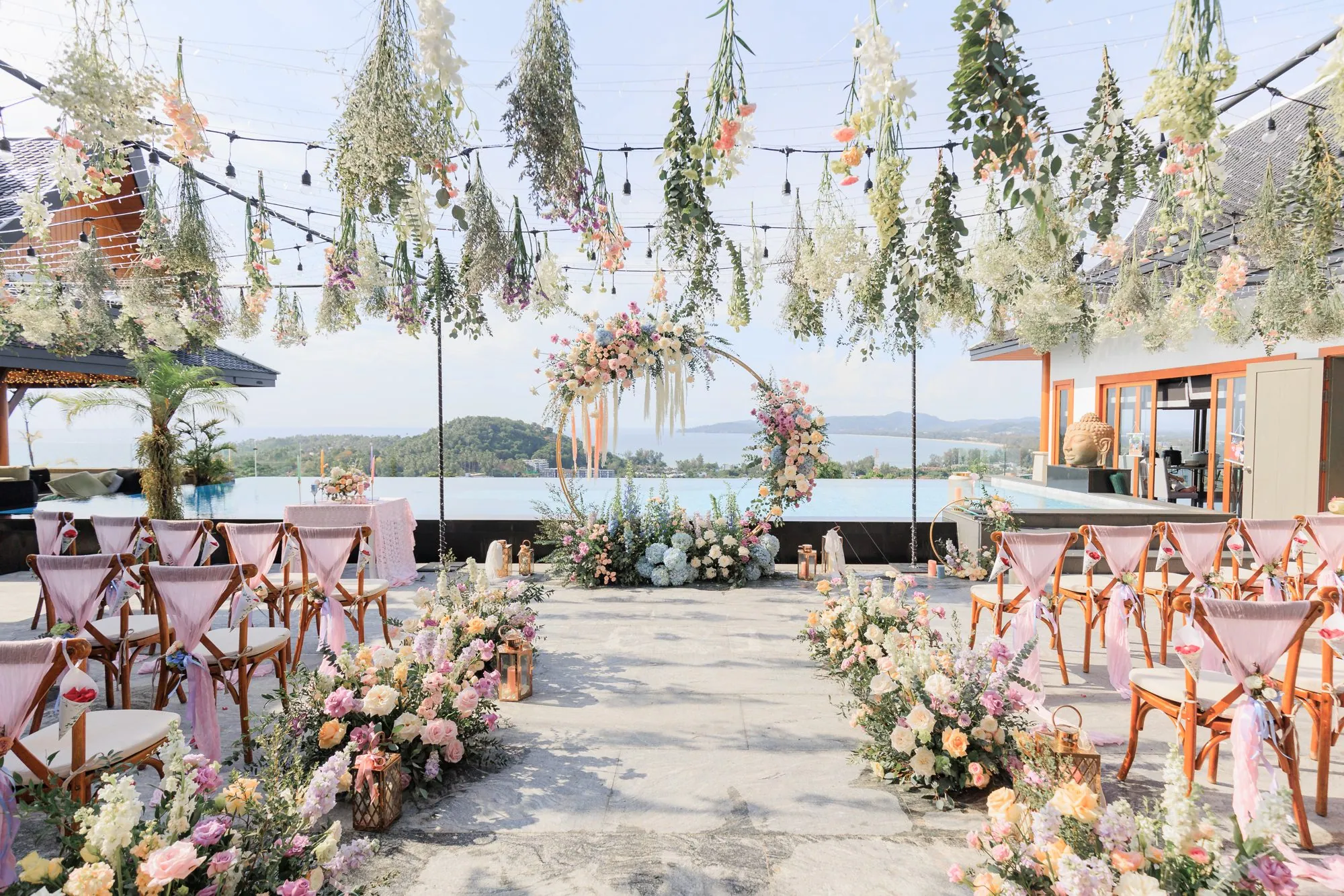 The ceremony aisle at Villa Baan Phu Prana on the morning of Ashleigh and James's wedding, with pastel florals and hanging installations framing the sea beyond