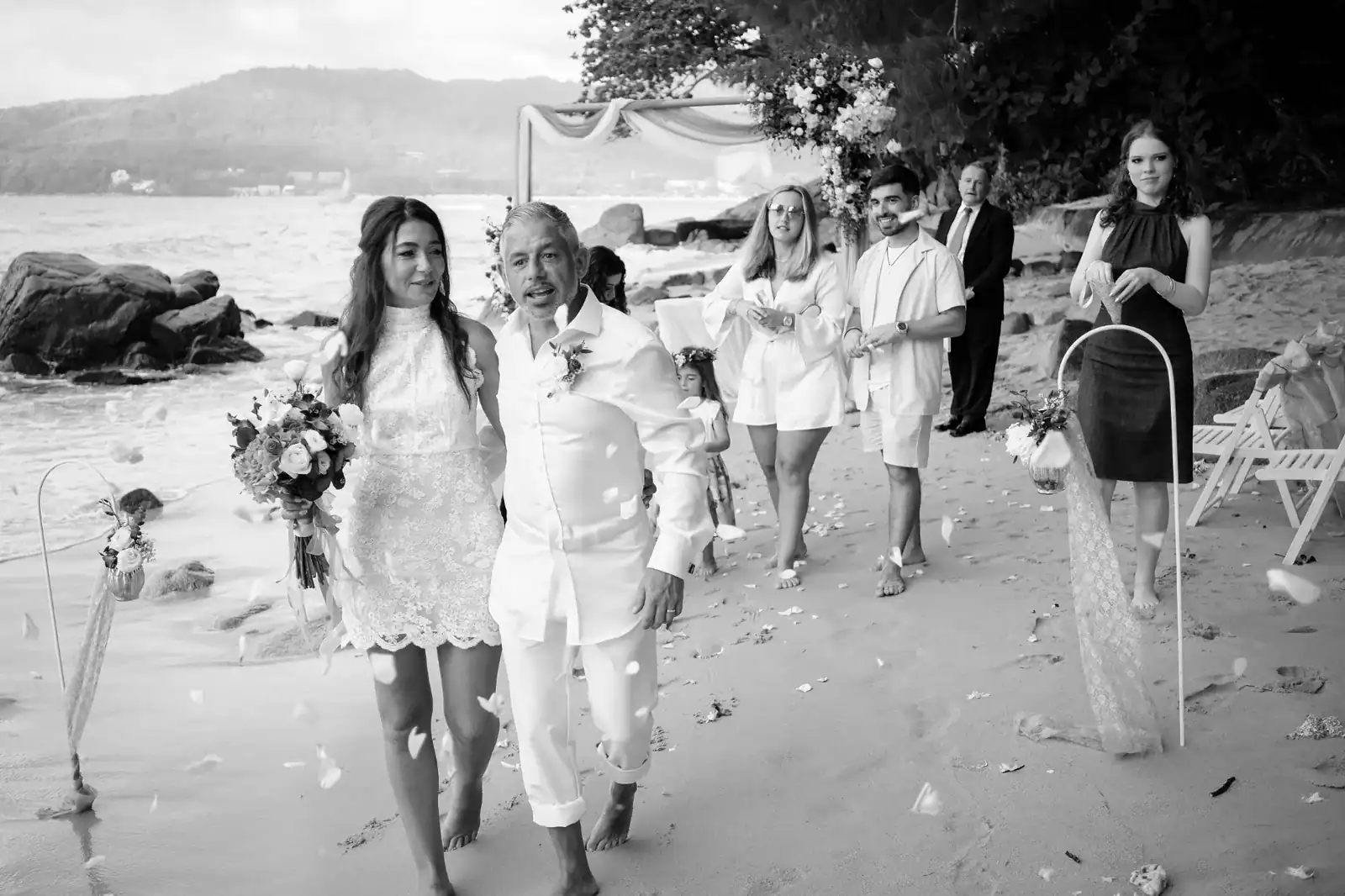 Couple walking along Hua Beach in Phuket after their vow renewal ceremony with guests and floral decorations