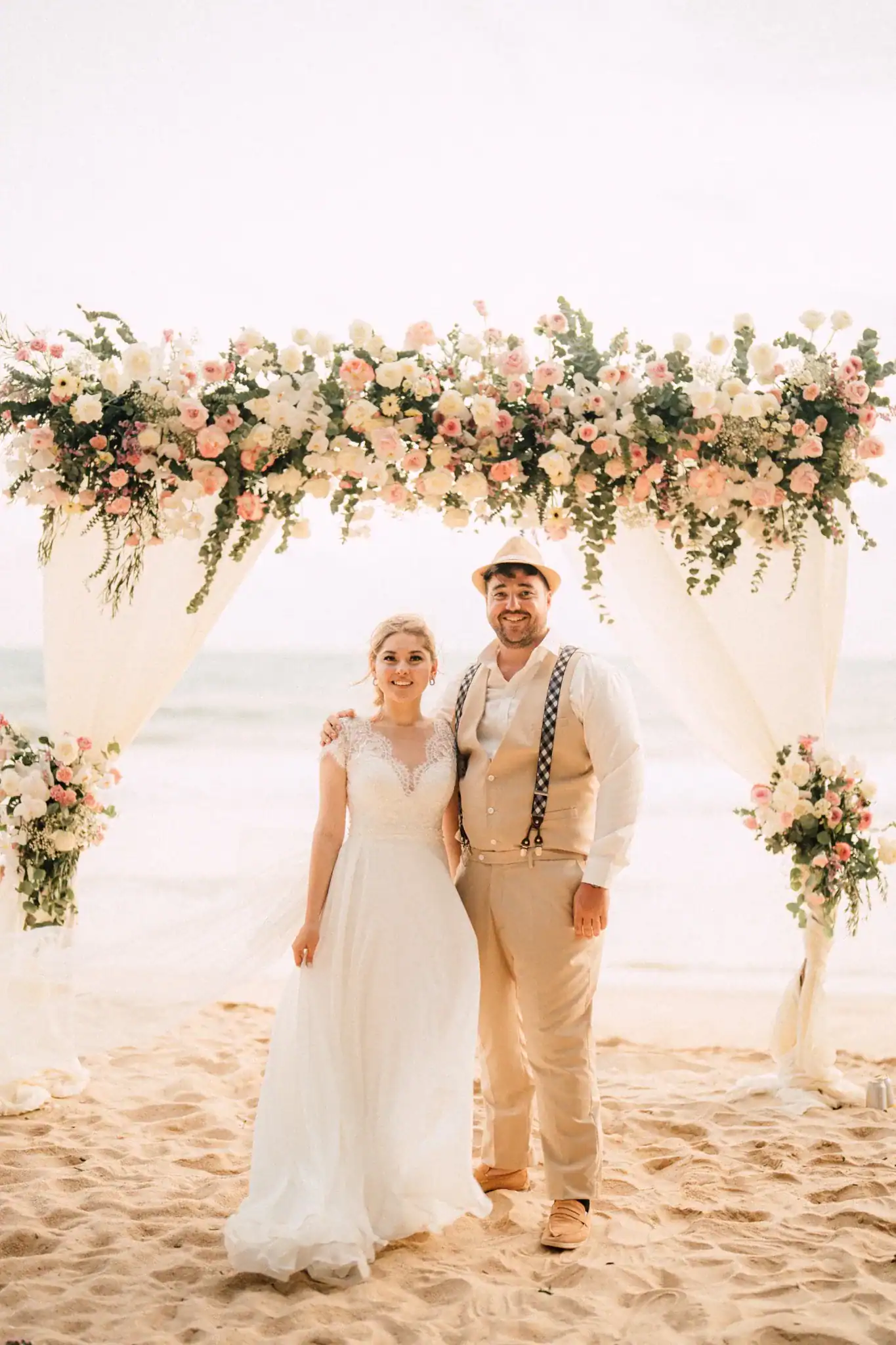 Bride and groom standing on Layan Beach in Phuket under a floral wedding arch during their beach elopement